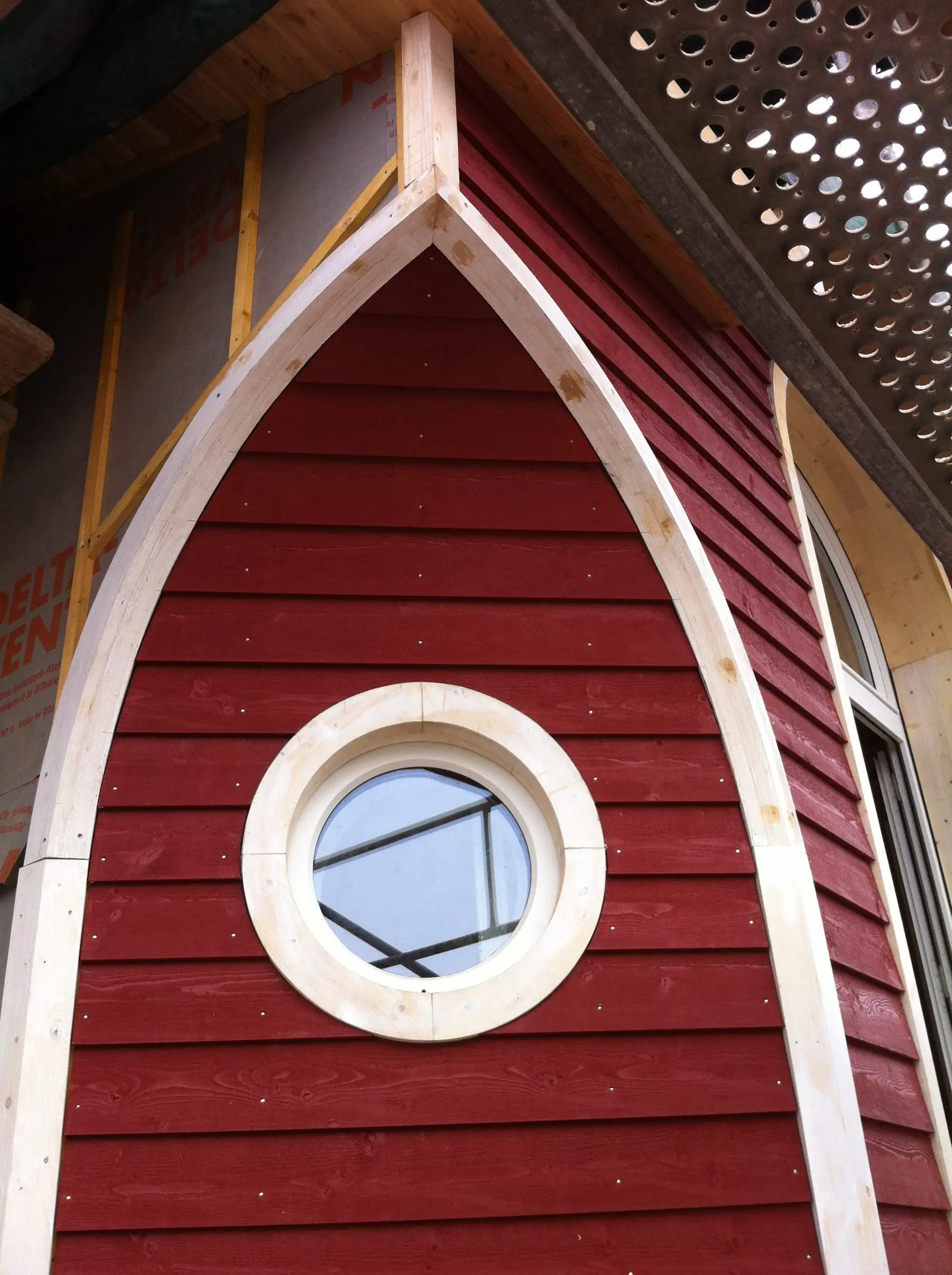 Pignon en bardage bois rouge percé d’un oculus rond.