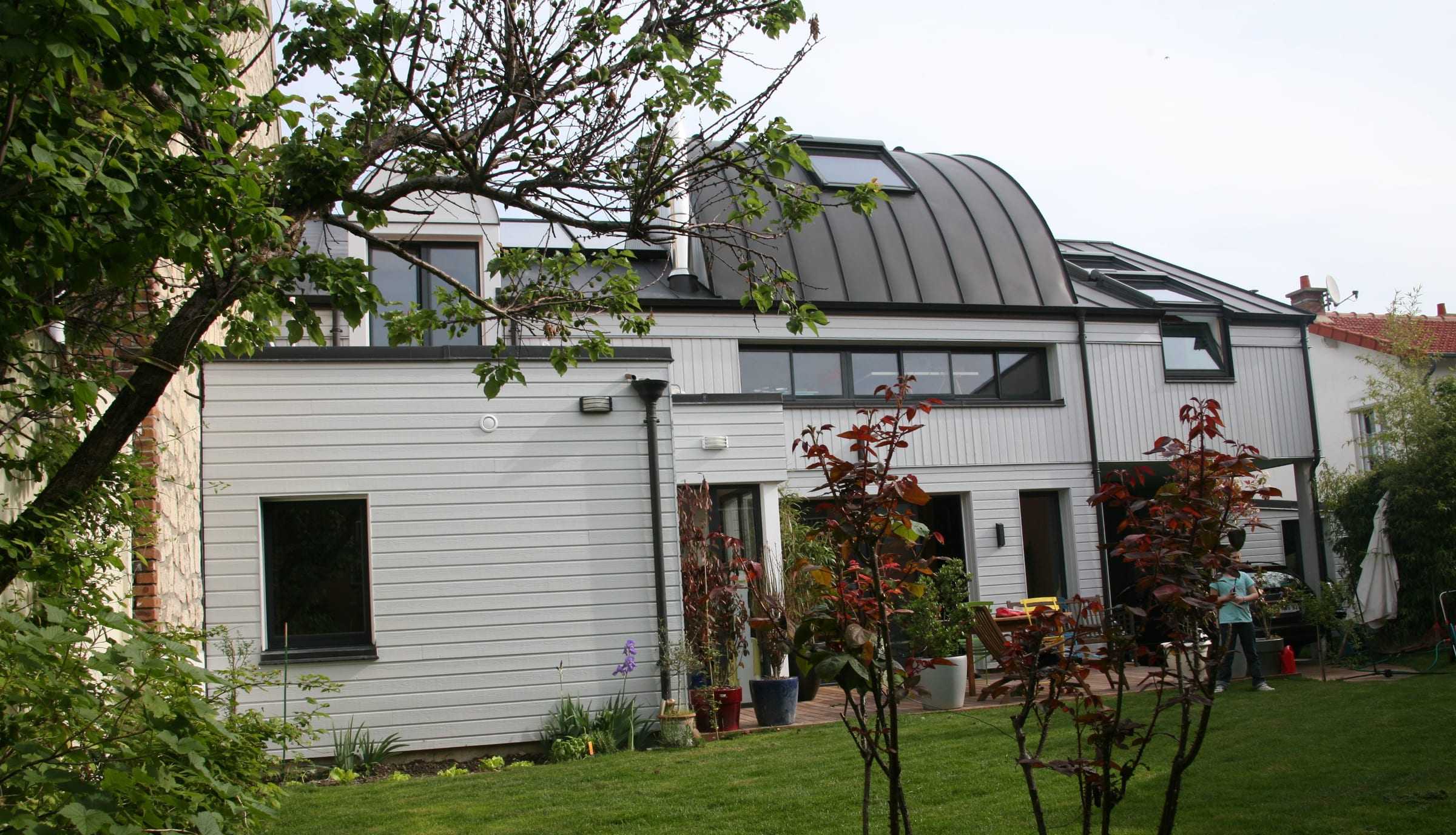 Maison à bardage blanc dont l’étage est couvert d’une toiture cintrée en zinc.